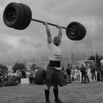 Paul Wood lifting an axle bar overhead during a strongman competition, showcasing his incredible strength and determination.